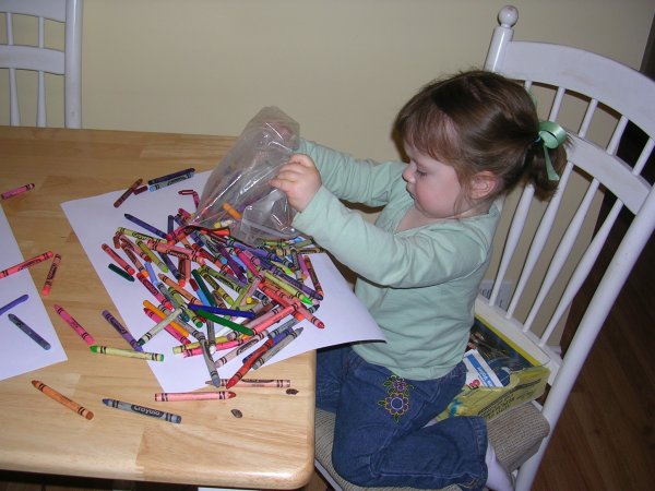 Young girl emptying a bag of crayons onto paper at a table