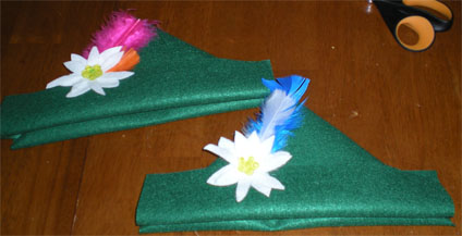 Two finished green felt Edelweiss hats with feathers and white flowers on a table
