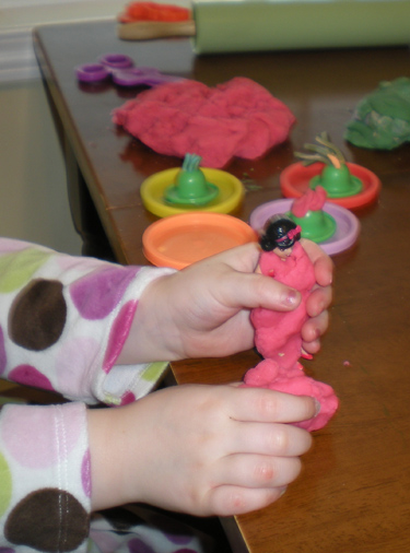 Child's hands shaping pink homemade playdough into a figure